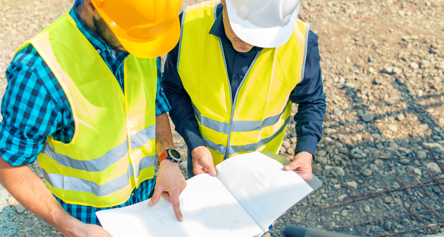 Construction Team on Site Reviewing Building Plans – Central MN Two construction workers in safety vests and helmets reviewing blueprints at an active job site